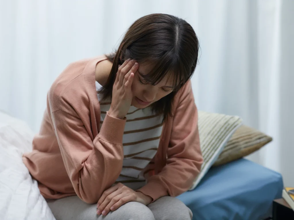 A woman with a headache massages her temples while seated on her couch.